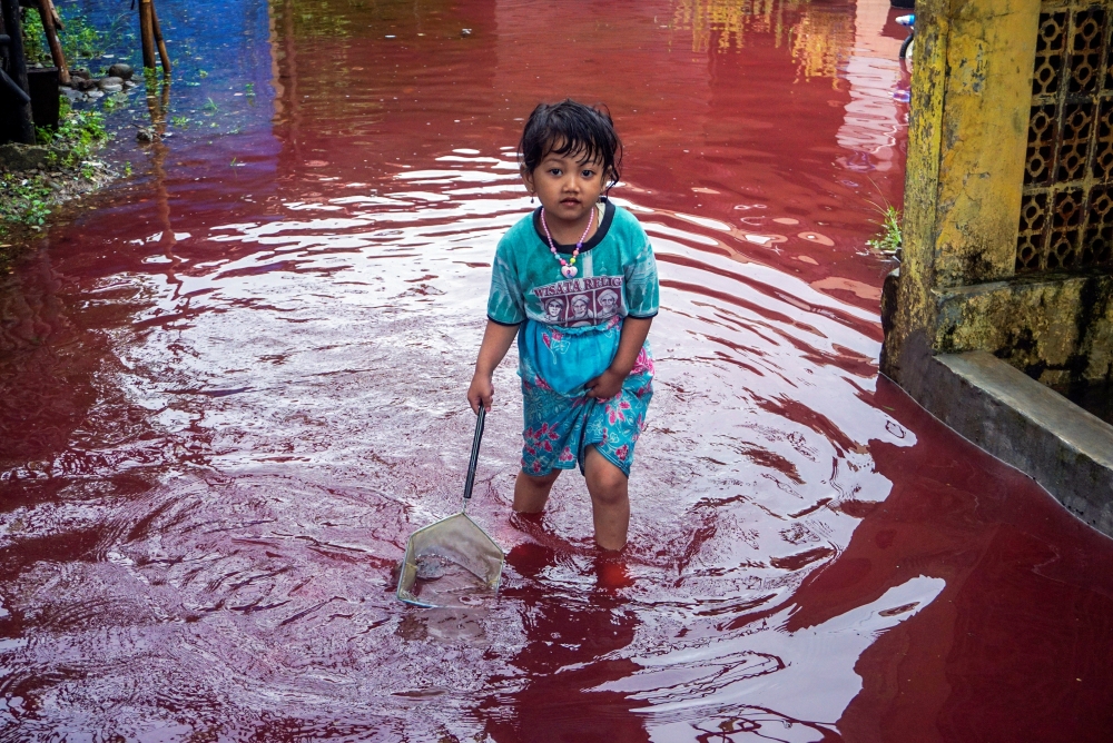 A girl walks through a flooded road with red water due to the dye-waste from cloth factories, in Pekalongan, Central Java province, Indonesia, February 6, 2021 in this photo taken by Antara Foto. Antara Foto/Harviyan Perdana Putra/ via Reuters 