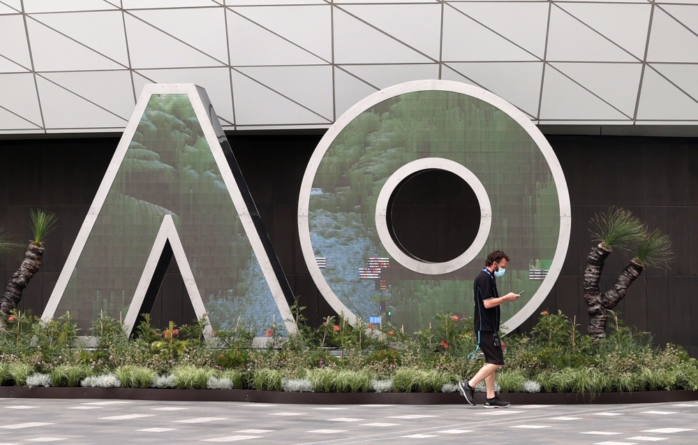 A man wearing a protective face mask walks past an Australian Open logo in Melbourne Park. Reuters/Loren Elliott