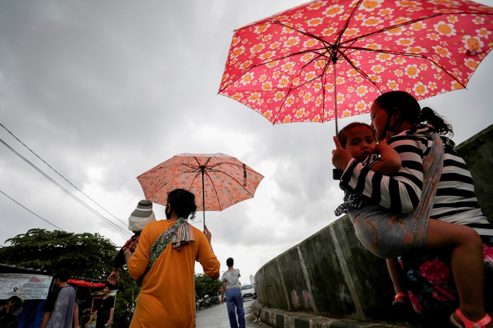 Women carrying children walk along a street affected by floods in Jakarta, Indonesia, February 8, 2021. REUTERS/Willy Kurniawan

