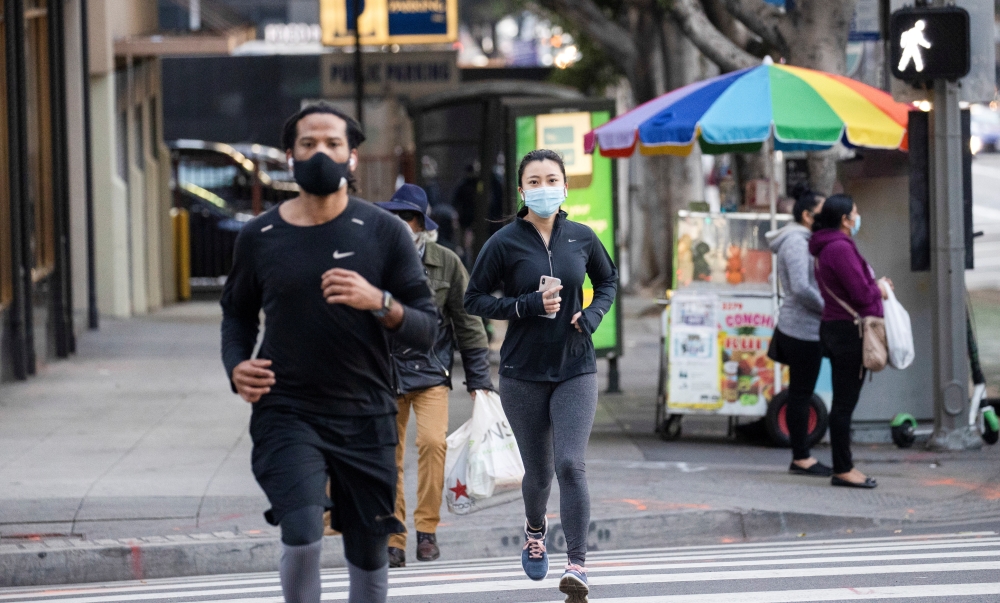 People wearing personal protective face masks jog downtown during the outbreak of the coronavirus disease (COVID-19), in Los Angeles, California, U.S., February 4, 2021. REUTERS/Mario Anzuoni
