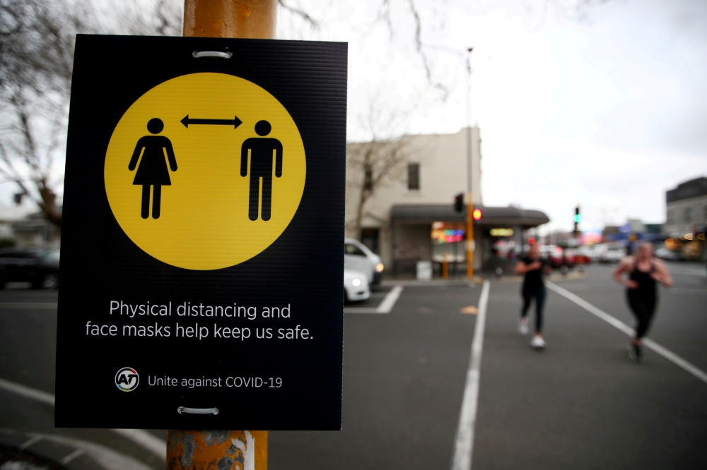 People jog past a social distancing sign on the first day of New Zealand's new coronavirus disease (COVID-19) safety measure that mandates wearing of a mask on public transport, in Auckland, New Zealand, August 31, 2020. REUTERS/Fiona Goodall//File Photo