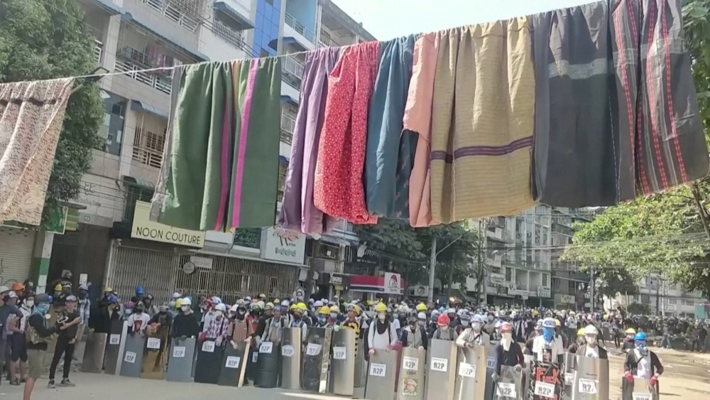 Traditional clothes hang on a rope as protesters holding shields stand in line in the background during a protest against the military coup in Yangon, Myanmar March 6, 2021 in this still image obtained by Reuters from a video.