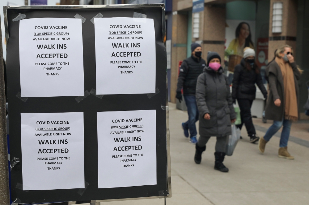 People wearing masks walk past a Shoppers Drug Mart store advertising coronavirus disease (COVID-19) vaccines, in Toronto, Ontario, Canada, March 16, 2021. REUTERS/Chris Helgren
