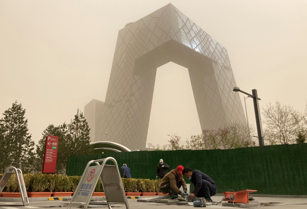 Construction workers are seen in front of the CCTV headquarters shrouded in dust as the city is hit by a sandstorm, in Beijing, China March 28, 2021. REUTERS/Martin Pollard