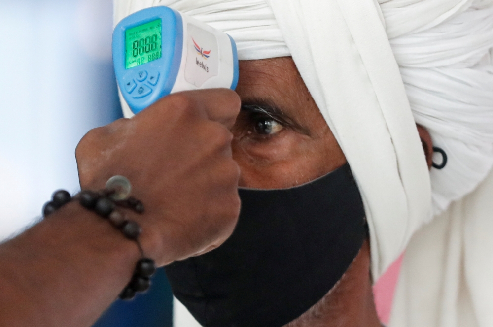  A health worker uses an infrared thermometer to check the temperature of a passenger amid the spread of the coronavirus disease (COVID-19), at a railway station in Mumbai, India, March 21, 2021. REUTERS/Francis Mascarenhas/File Photo