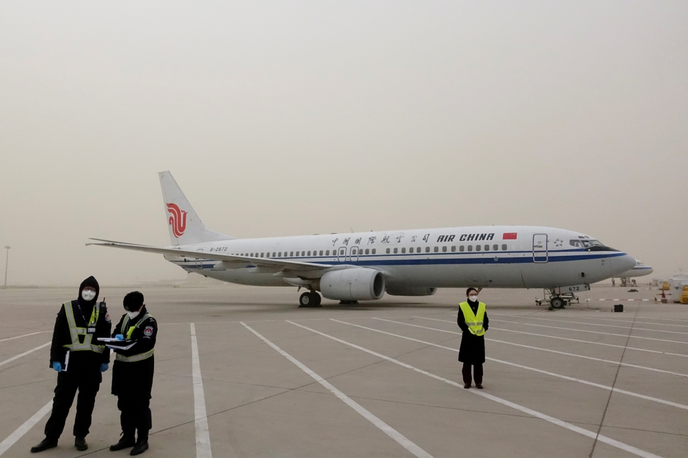 File photo: Staff members stand near a Boeing 737-800 airplane of Air China on the tarmac of Beijing Capital International Airport, which is shrouded in dust as the city is hit by a sandstorm, in Beijing, China March 28, 2021. Reuters/Carlos Garcia Rawlin