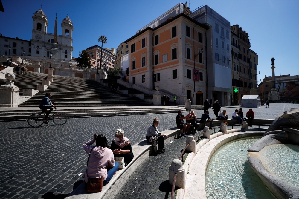 People wearing masks sit near the Spanish steps as COVID-19 restrictions in the Lazio region are slightly relaxed, in Rome, Italy March 30, 2021. REUTERS/Guglielmo Mangiapane
