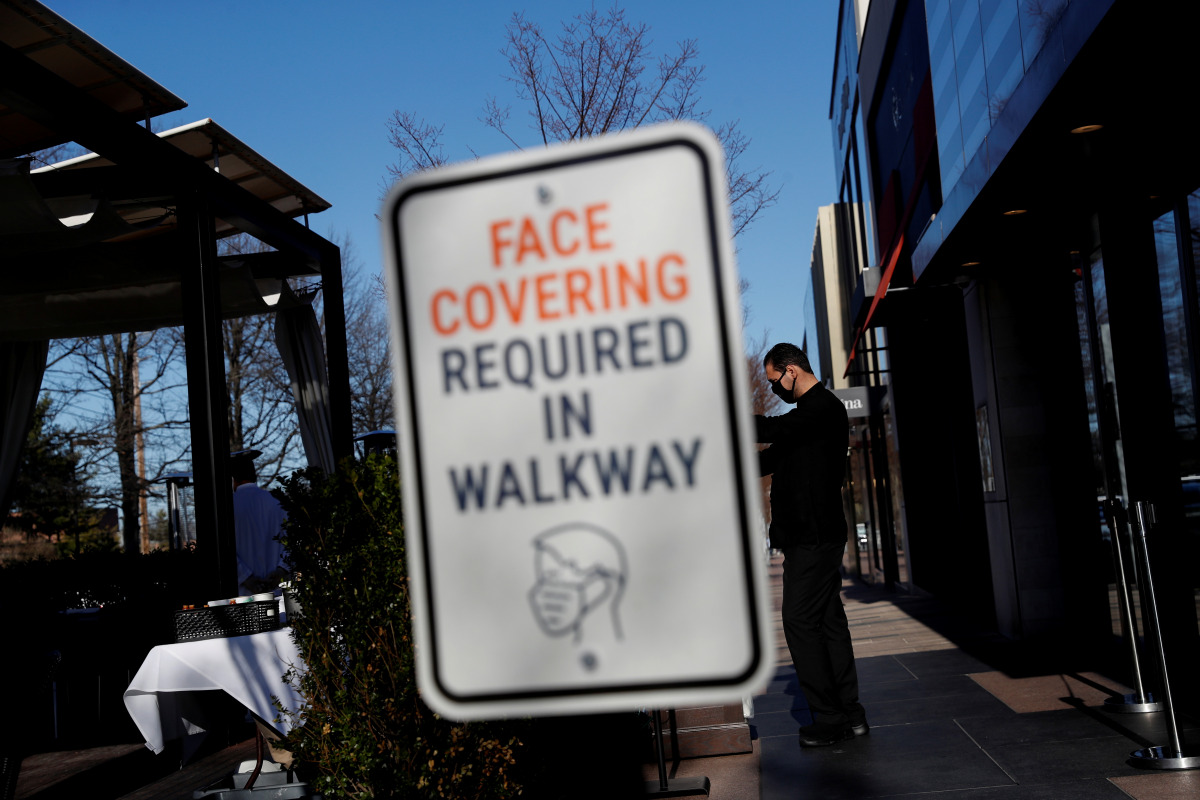 A sign requiring the wearing of a protective face mask is seen as a waiter stands outside a restaurant in Manhasset, New York, U.S. March 29, 2021. REUTERS/Shannon Stapleton

