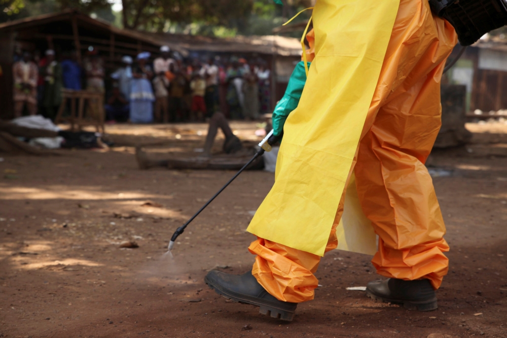 A member of the French Red Cross disinfects the area around a motionless person suspected of carrying the Ebola virus as a crowd gathers in Forecariah, Guinea, January 30, 2015. REUTERS/Misha Hussain/File Photo