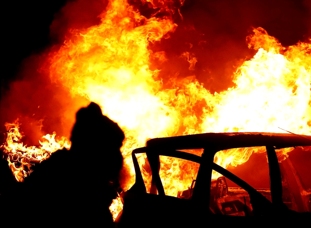 A rioter is seen near a burning car at the 