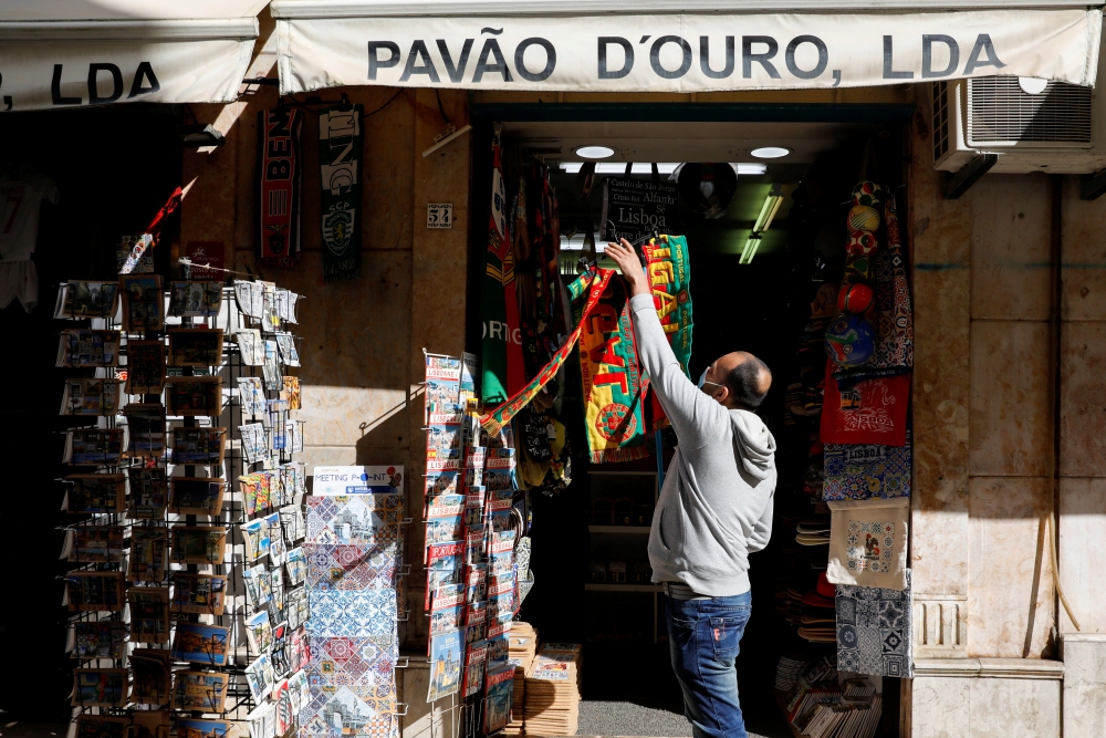 A man hangs football scarves in a store on the first day of the reopening after a country lockdown, amid the coronavirus disease (COVID-19) pandemic, in Lisbon, Portugal, April 5, 2021. REUTERS/Pedro Nunes/File Photo