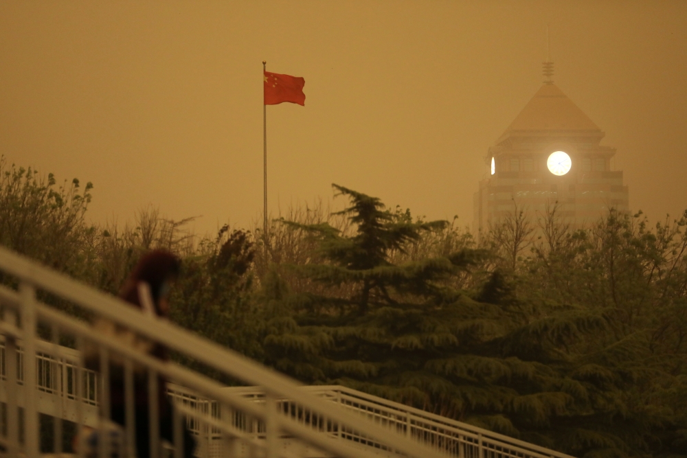 A pedestrian walks near a Chinese flag amid a duststorm in Beijing, China April 15, 2021. Reuters/Tingshu Wang
