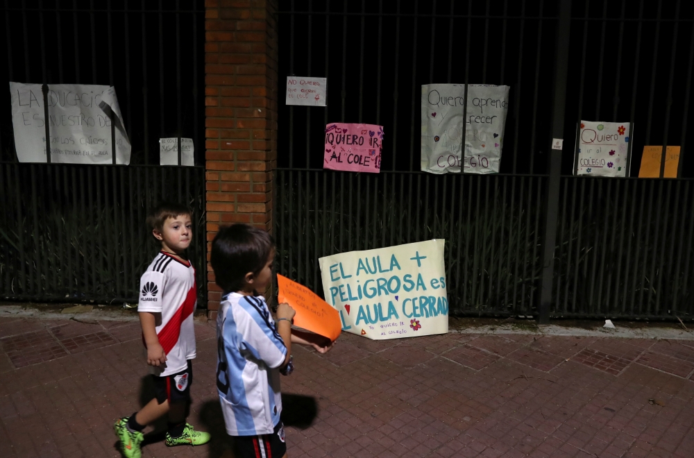 Children walk past placards during a protest outside the Olivos Presidential residence against new restrictions and the closure of schools imposed in the city and Buenos Aires' province amid a rise in coronavirus disease (COVID-19) cases, in Buenos Aires,