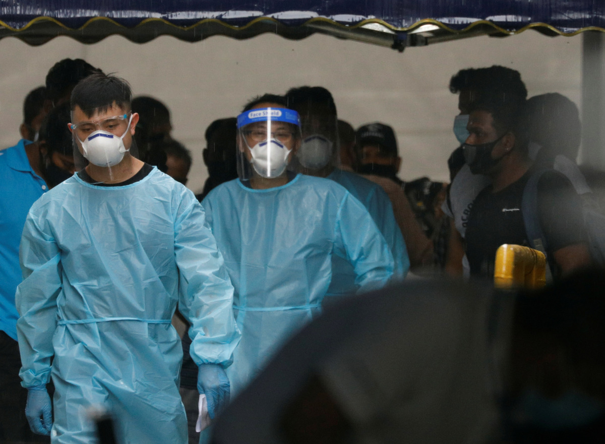 Personnel in protective garment usher a group of migrant workers to take a bus to a government quarantine facility after workers were tested positive for the coronavirus disease (COVID-19) at Westlite Woodlands dormitory in Singapore April 22, 2021. REUTE