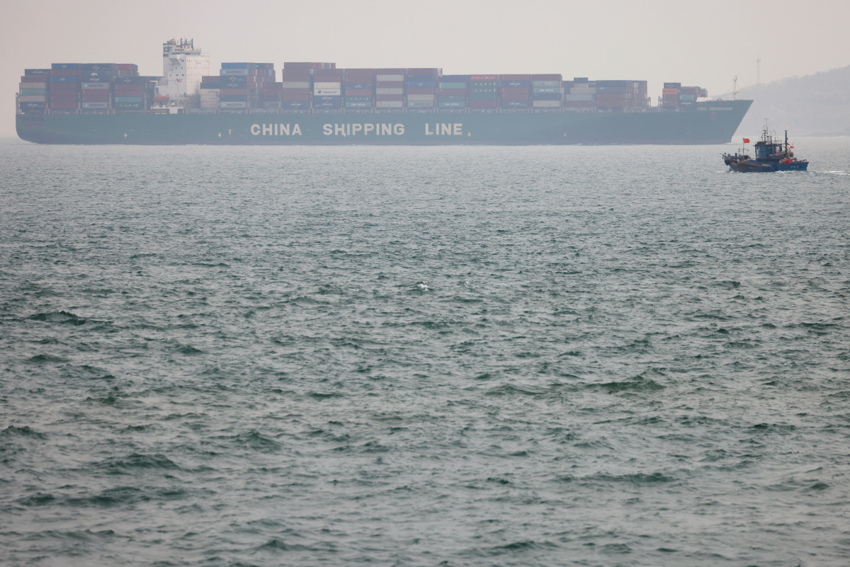 A fishing boat is seen near a China Shipping Container Lines (CSCL) vessel off the coast of Qingdao, Shandong province, China, following an oil spill in the Yellow Sea caused by a collision between tanker A Symphony and bulk vessel Sea Justice off Qingdao
