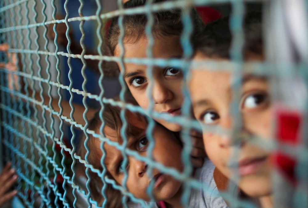 Palestinian children, who fled their homes due to Israeli air and artillery strikes, look through a window fence at a United Nations-run school where they take refuge, in Gaza City May 18, 2021. REUTERS/Suhaib Salem