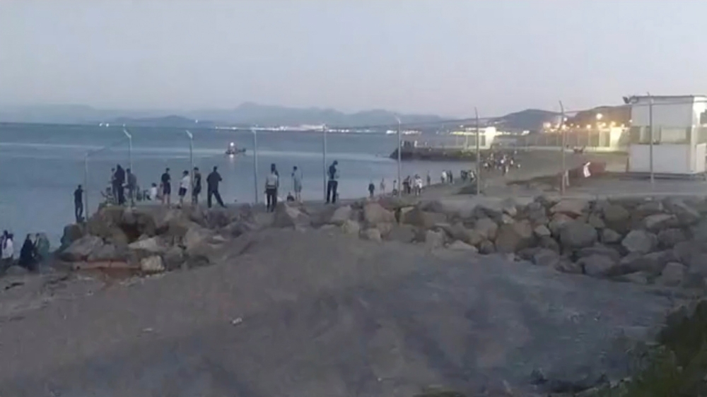 Migrants, who swam from Morocco to Spain, cross a fence on a beach in El Tarajal, Ceuta, Spain, May 17, 2021, in this still image from video obtained via social media. Ceuta Actualidad TV