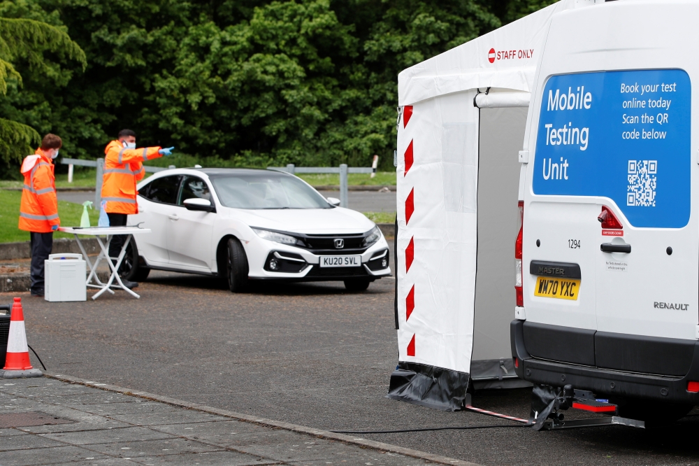 Staff members stand next to a car at a coronavirus disease (COVID-19) mobile testing unit at Oasis Beach Swimming Pool in Bedford, Britain May 25, 2021. Reuters/Paul Childs