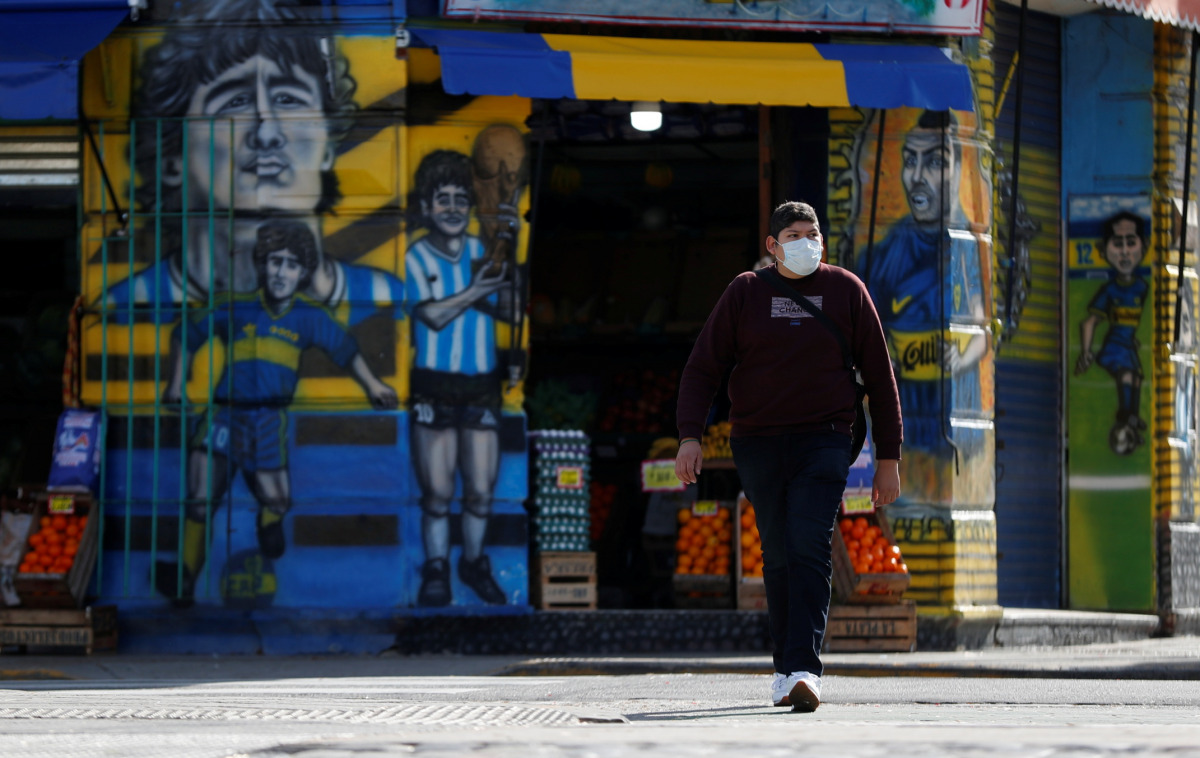 A man wearing a face mask as a preventive measure against the coronavirus disease (COVID-19) walks past a grocery store painted with graffitis depicting Diego Maradona, Carlos Tevez and Juan Roman Riquelme in Buenos Aires, Argentina May 31, 2021. REUTERS/