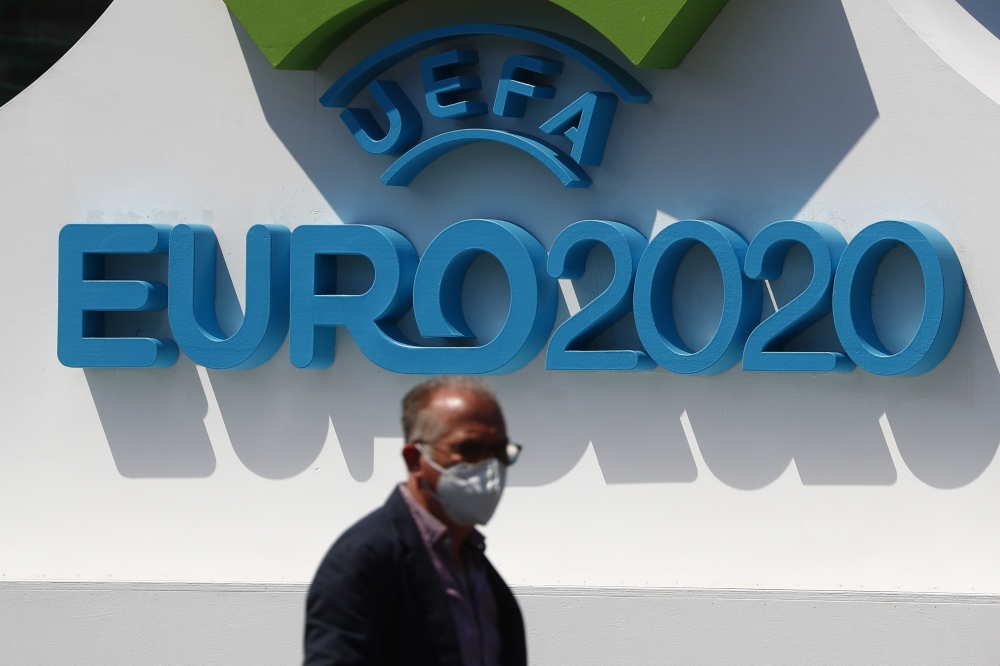 June 10, 2021 A man with a protective face-mask is seen in front of a Euro 2020 sign ahead of the opening match REUTERS/Guglielmo Mangiapane