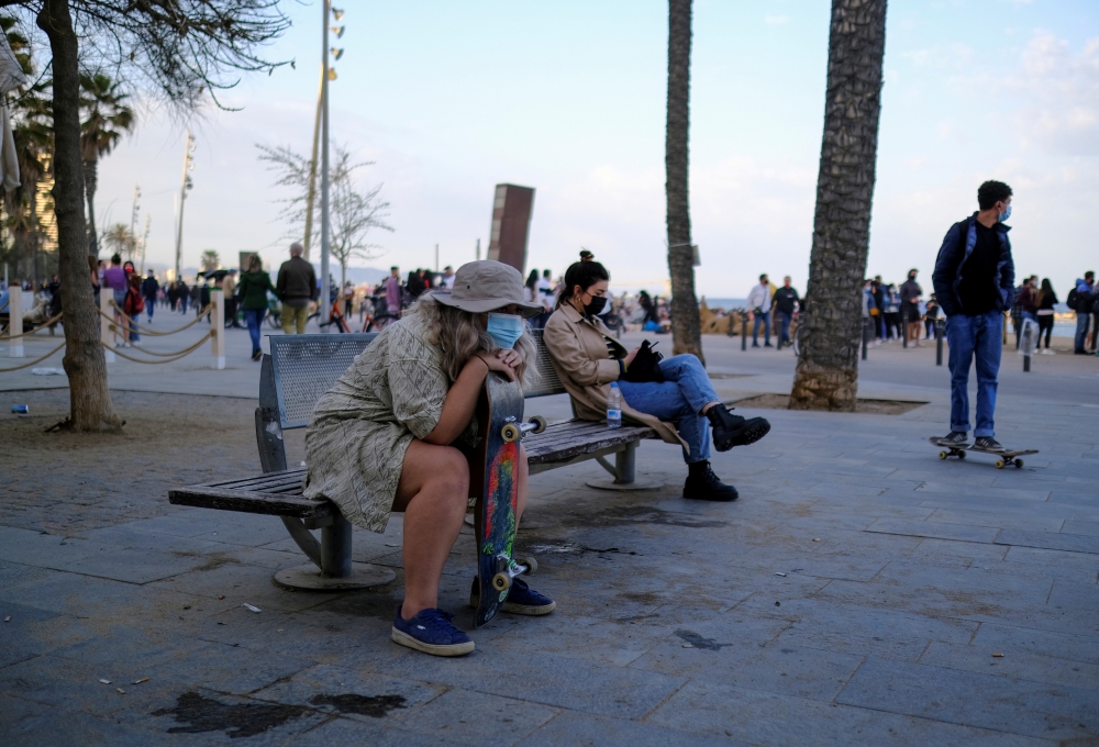 :FILE PHOTO: People wearing protective face masks sit on a bench in front of the Barceloneta beach, amid the coronavirus disease (COVID-19) outbreak, in Barcelona, Spain April 2, 2021. REUTERS/Nacho Doce/File Photo
