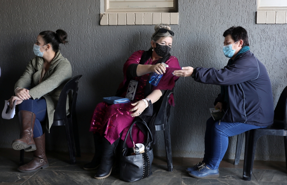A teacher sprays a colleague's hands with sanitizer as they wait to receive a dose of a coronavirus disease (COVID-19) vaccine during a vaccine rollout for teachers in Meyerton, south of Johannesburg, South Africa June 23, 2021. (REUTERS/Siphiwe Sibeko)