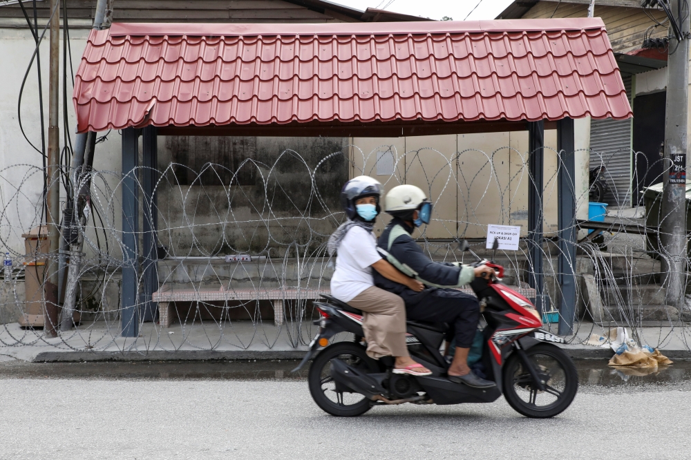 People wearing protective masks ride across a street outside an area under enhanced lockdown, amid the coronavirus disease (COVID-19) outbreak, in Kuala Lumpur, Malaysia June 29, 2021. REUTERS/Lim Huey Teng