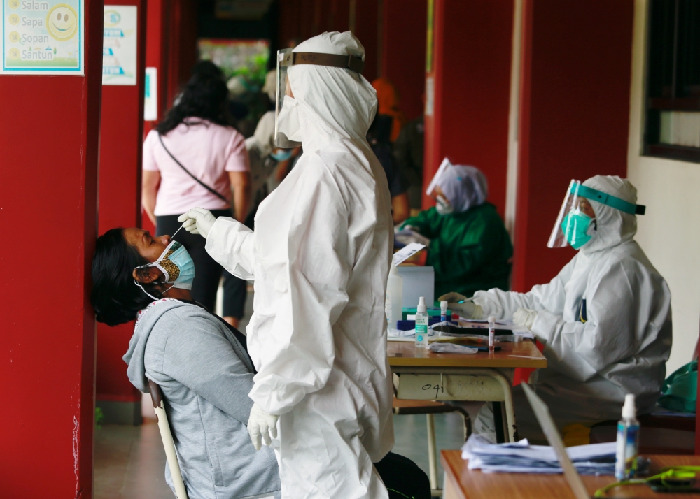 A healthcare worker in personal protective equipment takes a swab sample from a person to test for the coronavirus disease (COVID-19) during mass testing at a school in Jakarta, Indonesia, July 2, 2021. REUTERS/Ajeng Dinar Ulfiana