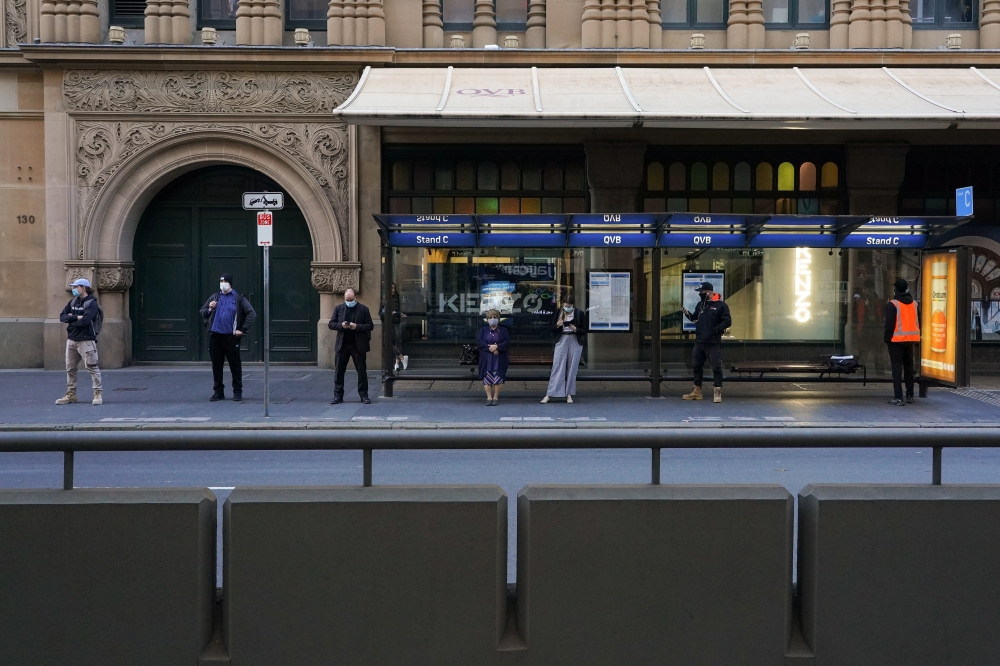 People wearing protective masks maintain social distance while waiting at a bus stop in the city centre during a lockdown to curb the spread of the coronavirus disease (COVID-19) in Sydney, Australia, July 5, 2021. REUTERS/Loren Elliott