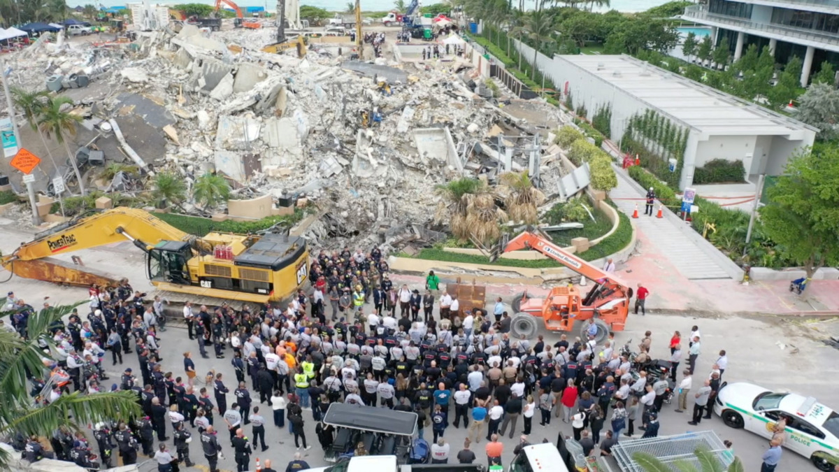 Members of the search and rescue team stand during a moment of silence and pray in front of the rubble of the collapsed Champlain Towers South building in Surfside, Florida, U.S. July 7, 2021, in this still image taken from drone footage obtained from soc