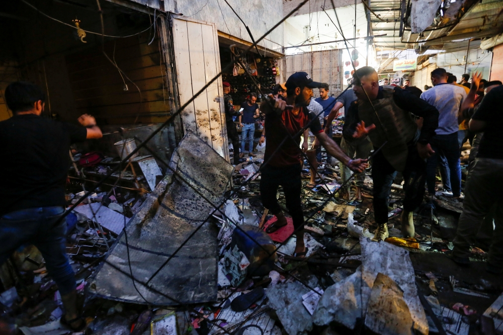 A man picks up debris as Iraqi security forces inspect the site of an explosion in Sadr City district of Baghdad, Iraq July 19, 2021. REUTERS/Wissam Al-Okaili
