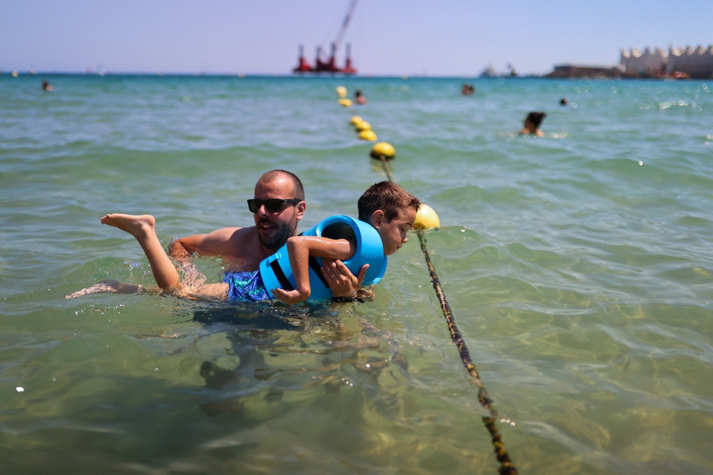 Disabled Max Segui, 7, accompanied by his father Albert Segui, 43, wears a life jacket as they swim in the Mediterranean sea, on Barcelona's Nova Icaria Beach, Spain, July 17, 2021. REUTERS/Nacho Doce