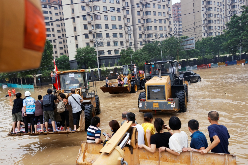 People ride on front loaders as they make their way through a flooded road following heavy rainfall in Zhengzhou, Henan province, China July 23, 2021. REUTERS/Aly Song