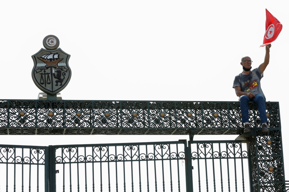 A supporter holds a Tunisian flag as he sits atop the gate of the parliament building in Tunis, Tunisia July 26, 2021. Reuters/Zoubeir Souissi
