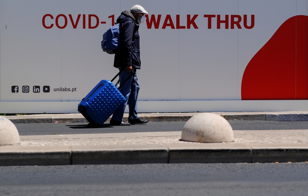 A man wearing a face mask pushes his luggage next to a Unilabs container where health technicians perform COVID-19 antigen tests for tourists and citizens in Lisbon, Portugal, July 29, 2021. REUTERS/Nacho Doce