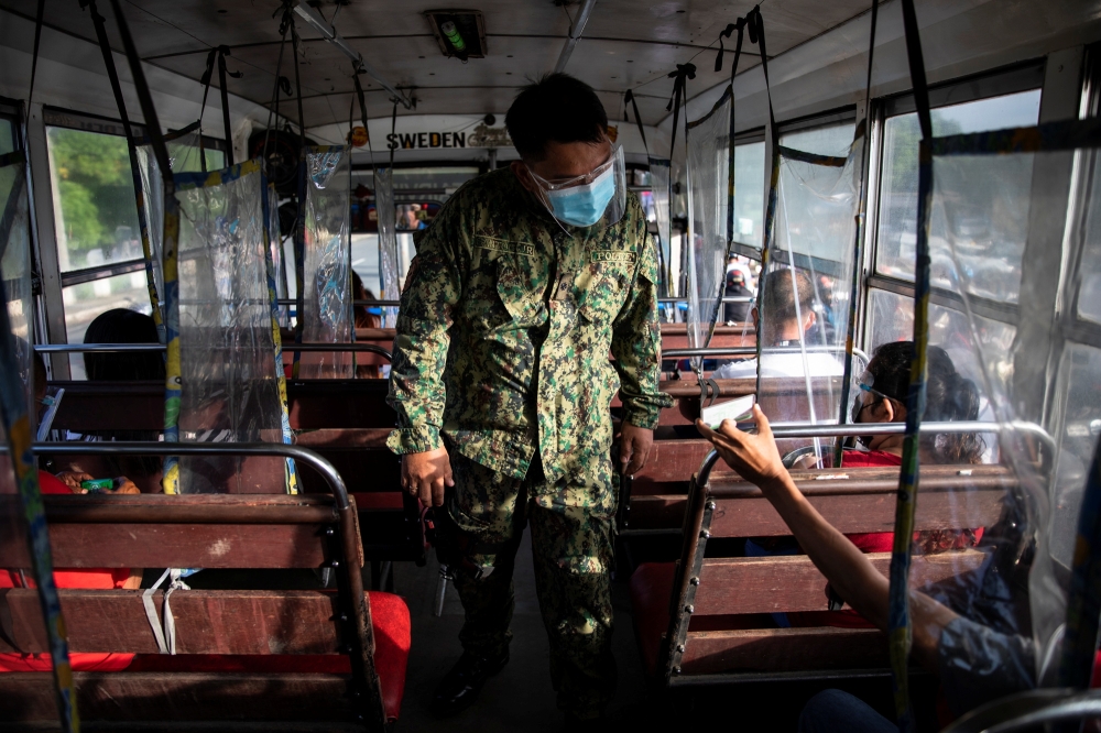 A policeman inspects an ID of a bus passenger passing through a checkpoint on the first day of a two-week lockdown to prevent the spread of the highly infectious coronavirus Delta variant, in Quezon City, Metro Manila, Philippines, August 6, 2021. Reuters