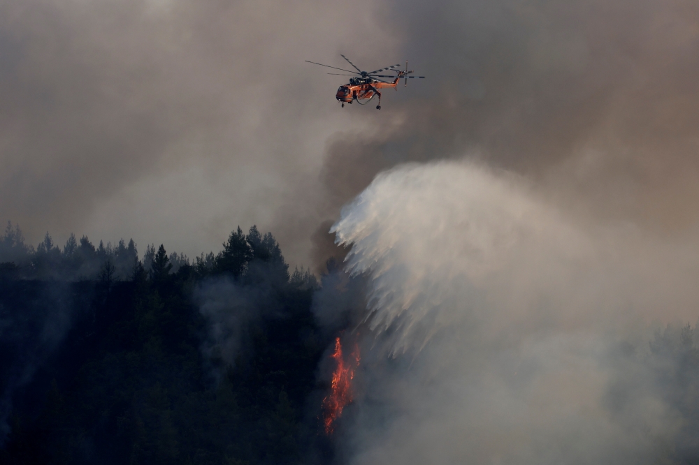 A firefighting helicopter makes a water drop as a wildfire burns in the village of Galatsona, on the island of Evia, Greece, August 10, 2021. REUTERS/Nicolas Economou