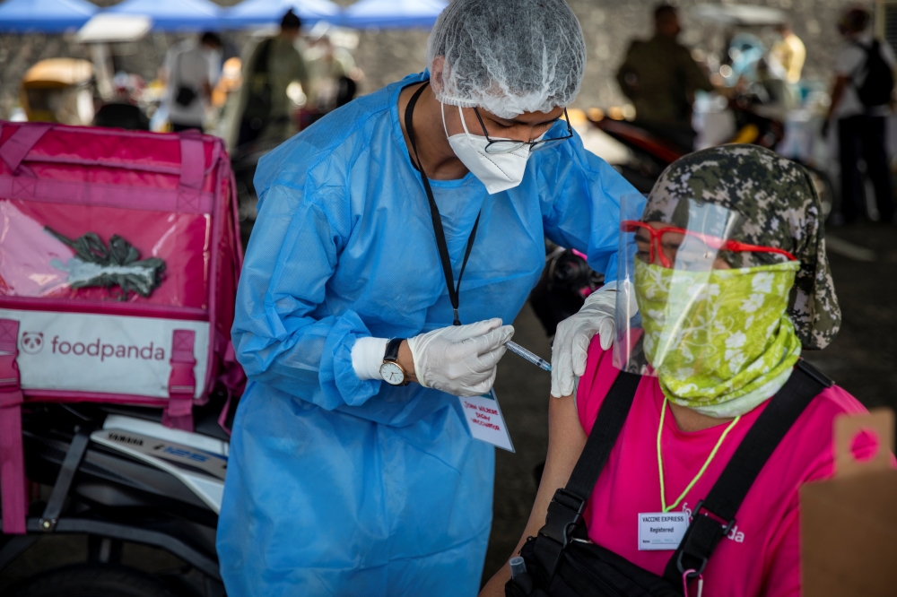 A health worker vaccinates a foodpanda delivery rider with Sinovac COVID-19 vaccine in a shopping mall's parking lot turned into a drive-thru vaccination site, in Quezon City, Metro Manila, Philippines, August 13, 2021. REUTERS/Eloisa Lopez