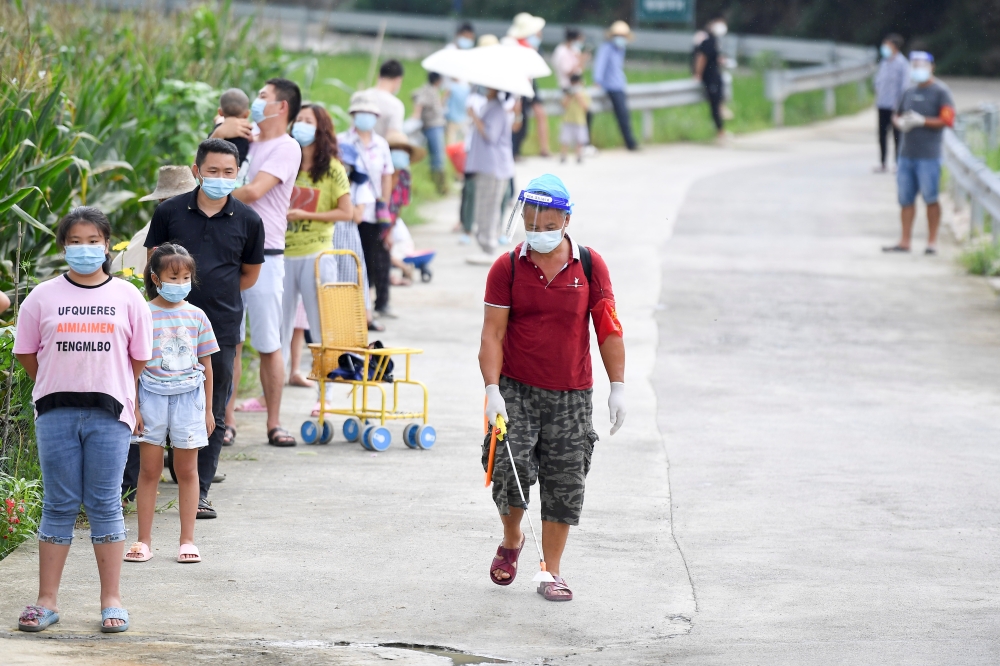 A worker disinfects next to villagers lining up by a corn field for nucleic acid testing at Baiyangping village following the coronavirus disease (COVID-19) outbreak in Zhangjiajie, Hunan province, China August 12, 2021. Picture taken August 12, 2021. cns
