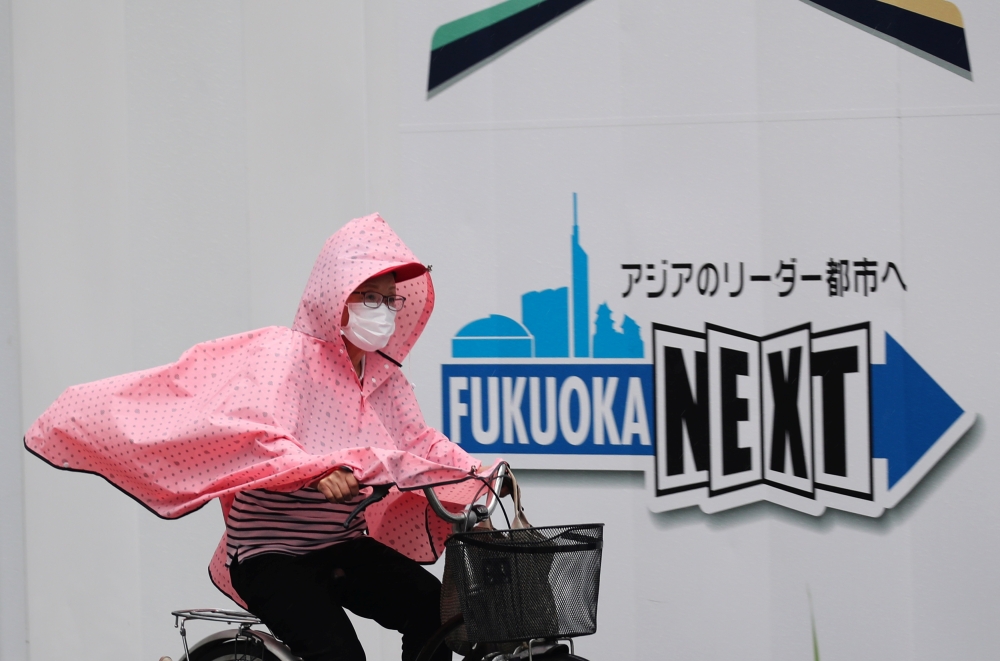 A woman wearing a protective mask and a rain coat, amid the coronavirus disease (COVID-19) outbreak, rides a bicycle in the rain in Fukuoka, Fukuoka Prefecture, Japan, August 17, 2021. REUTERS/Kim Kyung-Hoon