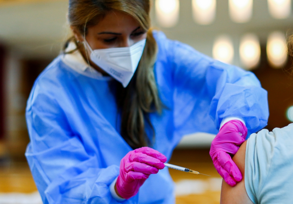 A medical worker in a school hall administers a dose of the Pfizer-BioNTech COVID-19 vaccine to a student of the Leibniz-Montessori secondary school, amid the coronavirus disease (COVID-19) pandemic, in Dusseldorf, Germany, August 27, 2021. REUTERS/Thilo 