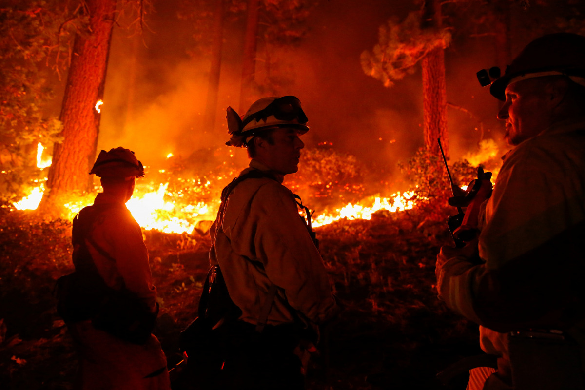 Matt Ziebarth (center), 45, a fire fighter with the El Dorado County Fire Department, and his colleagues, Darob Baker (left), 30, and fire captain Rob Sime, 44, work on structure protection along Santa Clause Drive as flames from the Caldor Fire burn thro