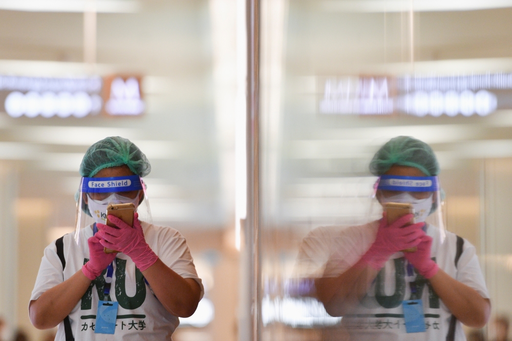 A person wearing a face shield and protective face masks uses her phone at the shopping mall on the first day of coronavirus restrictions lift on retail and dining in Bangkok and other high-risk areas to revive the economy, as the country battles its wors