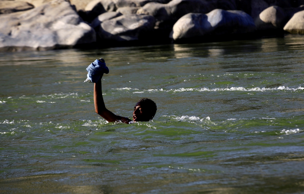 FILE PHOTO: An Ethiopian fleeing fighting in Tigray region lifts his clothes as he crosses the Setit river on the Sudan-Ethiopia border in Hamdayet village in eastern Kassala state, Sudan November 22, 2020. REUTERS/Mohamed Nureldin Abdallah
