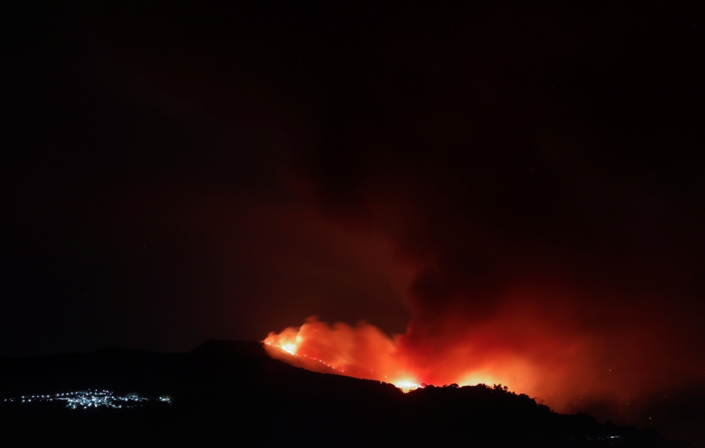 A wildfire is seen from a balcony near the town of Pujerra, which was evacuated, in Cartajima, near Estepona, Spain, September 12, 2021. REUTERS/Jon Nazca