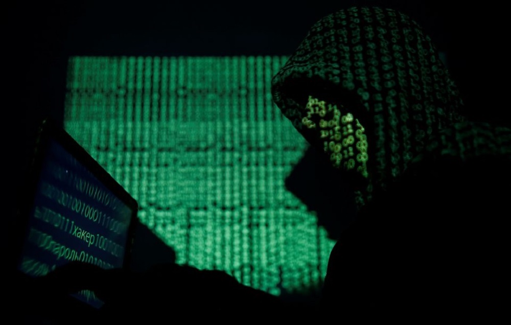 A hooded man holds a laptop computer as cyber code is projected on him in this illustration picture taken on May 13, 2017. REUTERS/Kacper Pempel/Illustration