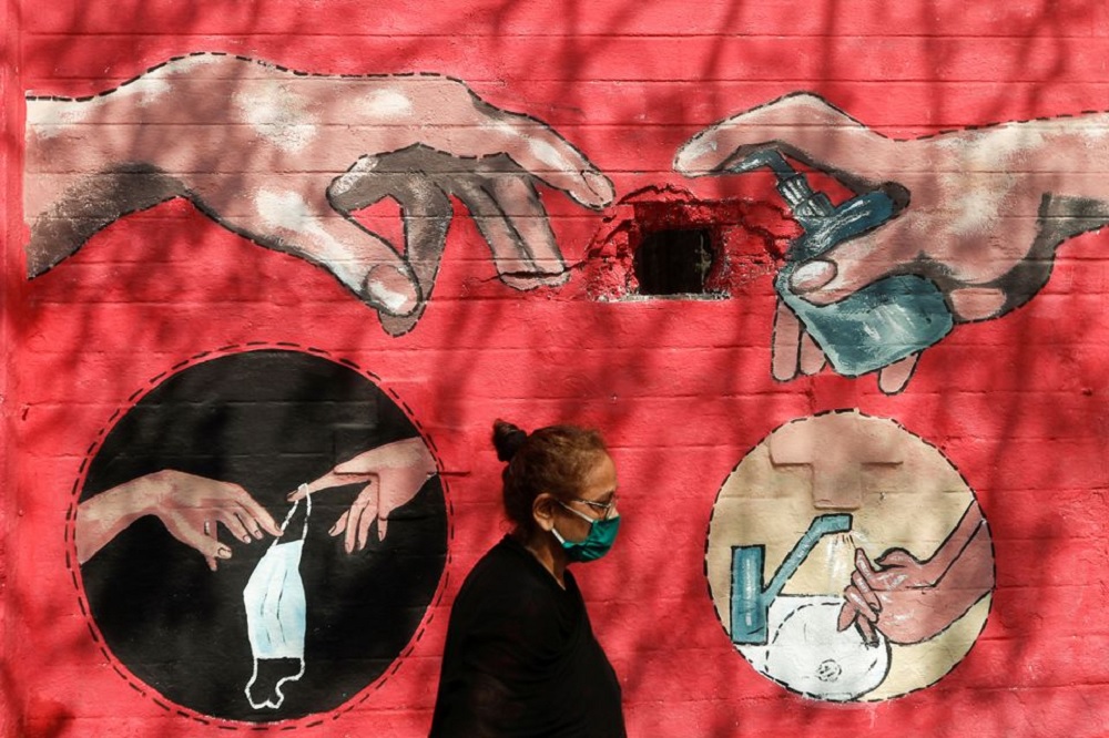 A woman walks past a graffiti, on a street, amidst the spread of the coronavirus disease (COVID-19) in Mumbai, India, April 6, 2021. REUTERS/Francis Mascarenhas/File Photo
