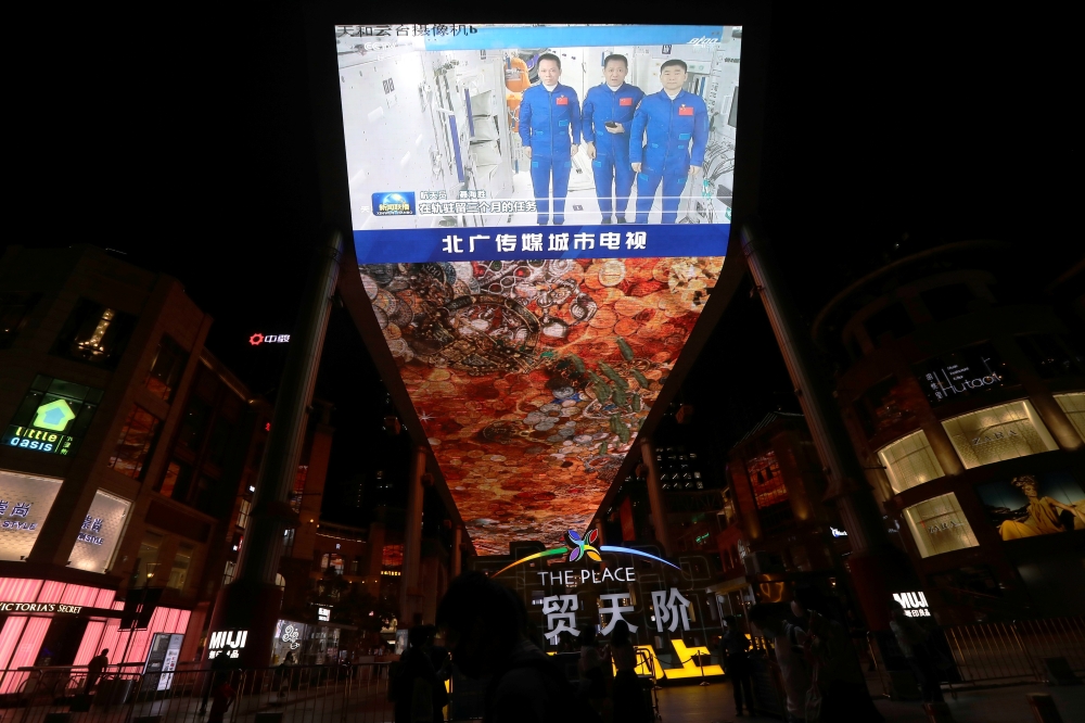 A giant screen shows a news broadcast of the astronauts of the Shenzhou-12 mission inside the core module Tianhe of the Chinese Space station, before returning to Earth, in Beijing, China September 16, 2021. REUTERS/Tingshu Wang