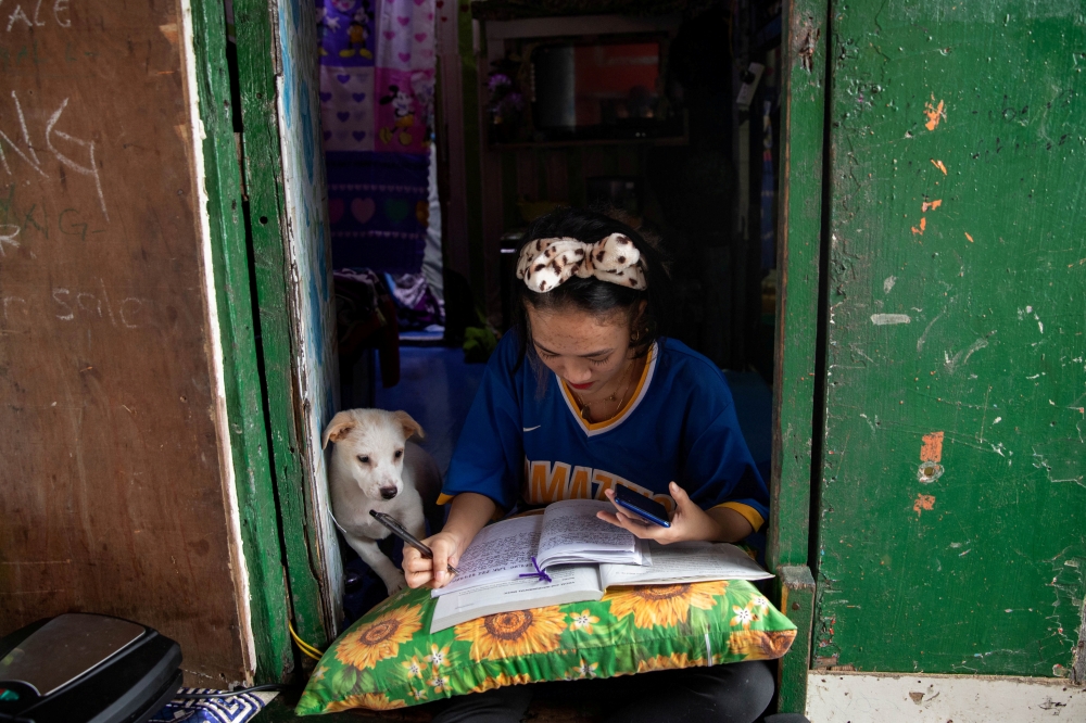 Annie Sabino, 16, a grade 9 student, completes her school work next to her dog, while tending to her family's sidewalk eatery beside their home, as schools remain closed during the coronavirus disease (COVID-19) outbreak, in Manila, Philippines, January 6