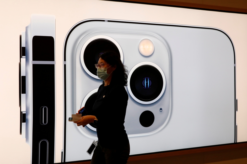 An Apple employee wearing a face mask walks past an image of an iPhone 13 Pro at an Apple Store on the day the new Apple iPhone 13 series goes on sale, in Beijing, China, September 24, 2021. REUTERS/Carlos Garcia Rawlins/File Photo